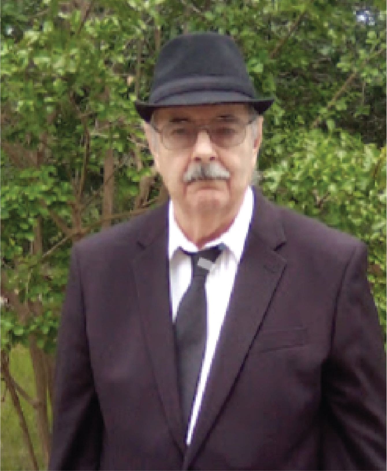 A well-dressed man standing amidst trees, wearing a suit and tie, exuding professionalism and elegance